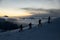 Silhouettes of four skiers with poles walking down the slope