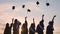 Silhouettes of graduates toss their caps at sunset.