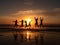 Silhouettes of a group of people on the beach, joyfully jumping up against the backdrop of the setting sun. The scene is