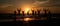 Silhouettes of a group of people on the beach, joyfully jumping up against the backdrop of the setting sun. The scene is