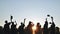 Silhouettes of Happy college graduates tossing their caps up at sunset.