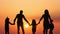 Silhouettes of happy family walking together in the meadow during sunset.