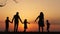 Silhouettes of happy family walking together in the meadow during sunset.