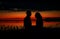 Silhouettes of lovers couple hugging at sunset, sunrise against the backdrop of the sea, sun, clouds in fiery red, orange colors