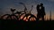 Silhouettes of the loving couple tenderly kissing in the field during the red and gray sunset. Walk with bicycles