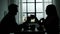 Silhouettes of man and woman clinking glasses at kitchen table talking drinking