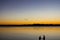 Silhouettes of man and woman fishing with sunset reflecting in water and flock of birds flying in formation overhead