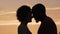 Silhouettes of man and woman gently touching each other, sunset background