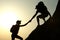 Silhouettes of man and woman helping each other to climb on hill