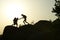 Silhouettes of man and woman helping each other to climb on hill