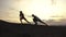 Silhouettes of mixed race couple of fitness instructors doing exercises outdoor at the rocky mountains background on