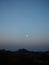 The silhouettes of mountains and trees under the dusk moon