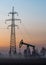 Silhouettes of oil pump and high-voltage transmission line support in morning fog at sunrise