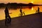 Silhouettes of one girl and two boys with bikes on river coast at sunset.
