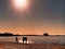 Silhouettes of people and  family couple  walking  on the beach sand at sunset on sea on horizon ship in harbor ,reflection of sun
