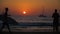 Silhouettes of people walking along the beach at sunset. Ships on the horizon.