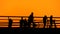 Silhouettes of people are walking on the pier against clear orange sunset sky