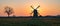 Silhouettes of a solitary tree and dutch windmill against an orange sky.