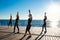 Silhouettes of sportive girls dancing zumba near sea at sunrise.