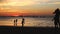 Silhouettes on a sunset background on a tropical beach. Family, father and son play badminton, daughter takes selfie.