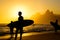 Silhouettes of surfers holding their surfboards on the background of golden sunset on Ipanema Beach , Rio de Janeiro