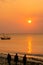 Silhouettes of three Masai in traditional clothes standing on the beach, during orange sunset, with calm sea view, Zanzibar