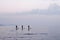 Silhouettes of three people float on  surfboard on a calm sea at dusk