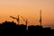 The silhouettes of three tower cranes and houses during sunset, sunset with an orange sky in the city