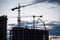 Silhouettes of tower cranes and builders in action on sunset background. Workers during formwork and pouring concrete through a Ñ