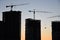 Silhouettes of tower cranes constructing a new residential building at a construction site against sunset background