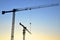 Silhouettes of tower cranes constructing a new residential building at a construction site against sunset background. Renovation