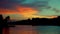 Silhouettes of trees against sky over tranquil river in the evening.