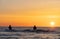 The silhouettes of two anglers in waterproof trousers fishing in front of a dreamy orange sunset in the Baltic Sea.