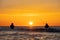 The silhouettes of two anglers in waterproof trousers fishing in front of a dreamy orange sunset in the Baltic Sea.