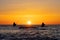 The silhouettes of two anglers in waterproof trousers fishing in front of a dreamy orange sunset in the Baltic Sea.