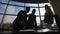 Silhouettes of two businessmen working with a computer on a window background in a big bright office