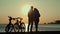 The silhouettes of two people with bicycles on the beach