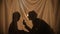 Silhouettes of woman and boy shining flashlight and catching light beams. Mom and little son sitting behind curtain at