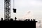 Silhouettes of workers and construction crane with cargo against the sky