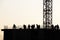 Silhouettes of workers and tower crane on construction site against the sky