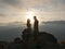 Silhouettes of young couple standing on a mountain and looking to each other on beautiful sunset background. Love of guy