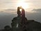 Silhouettes of young couple standing on a mountain and looking to each other on beautiful sunset background. Love of guy