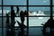 Silhouettes of young family standing at the window and look at the airport strip with airplanes and waiting for their