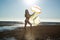 Silhoutte of a pretty senior Asian female in a swimming suit standing and hold umbrella and flaunt yellow fabric on the beach.