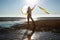 Silhoutte of a pretty senior Asian female in a swimming suit standing and hold umbrella and flaunt yellow fabric on the beach.