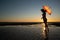 Silhoutte of a pretty senior Asian female in a swimming suit standing and hold umbrella posing on the beach.