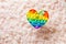 Silicone rainbow antistress toy in the shape of a heart on a background of fluff. Trendy relaxation tool