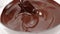 Silicone spatula stirs dark melted chocolate in glass bowl slow mo close up