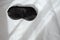 Silk black sleep mask without inscription on white rumpled sheets. Top view, flat lay. Horizontal. Copy spase. Concept of rest,