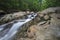 Silky water rushing over eroded rocks with green forest in background